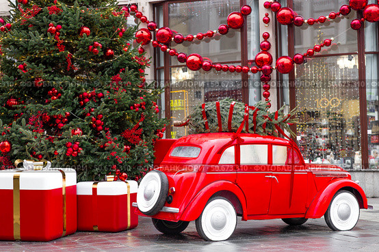 A vintage red Christmas car is carrying a Christmas tree on its roof. Decorated New Year's Moscow. Product delivery concept. Стоковое фото, фотограф Photojuli / Фотобанк Лори
