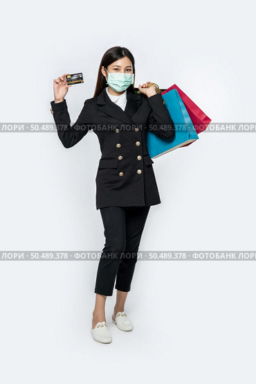 A woman in black and wearing a mask walks shopping, carries credit cards, and lots of bags. Стоковое фото, агентство Ingram Publishing / Фотобанк Лори