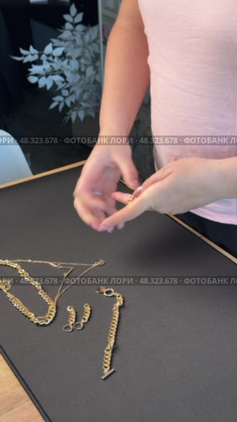 A woman reviewing jewelry, laying out a gold-colored necklace, bracelet, earrings, and ring on a table. Vertical video. Oblique Angle. Стоковое видео, видеограф Vadzim Yakubovich / Фотобанк Лори