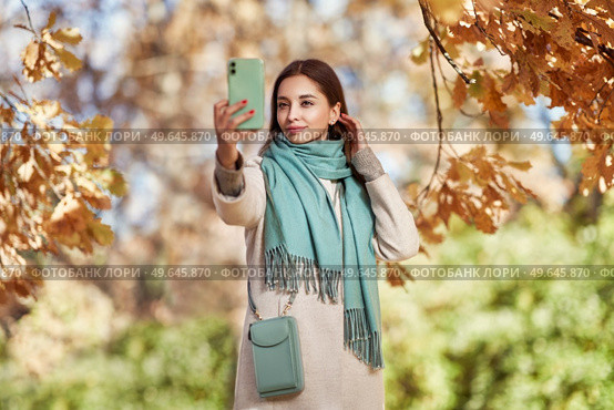 A young beautiful woman walks through the autumn park. A girl with a smartphone takes photos in an autumn forest. Стоковое фото, агентство Ingram Publishing / Фотобанк Лори