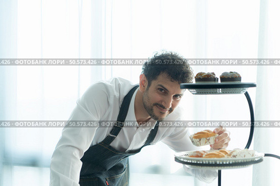 A young man puts on an apron to make dessert to eat with his wife. Checking the completeness of the finished dessert. Стоковое фото, агентство Ingram Publishing / Фотобанк Лори