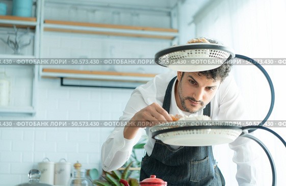 A young man puts on an apron to make dessert to eat with his wife. Checking the completeness of the finished dessert. Стоковое фото, агентство Ingram Publishing / Фотобанк Лори