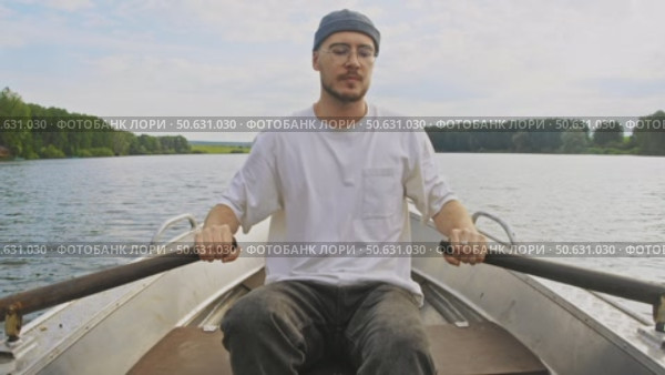 A young man skillfully navigates a boat with powerful strokes of his oars in a pond. Стоковое видео, видеограф Strunov David / Фотобанк Лори