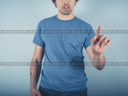 A young man wearing a blue t-shirt is raising his finger to either point or swipe or push. Стоковое фото, агентство Ingram Publishing / Фотобанк Лори