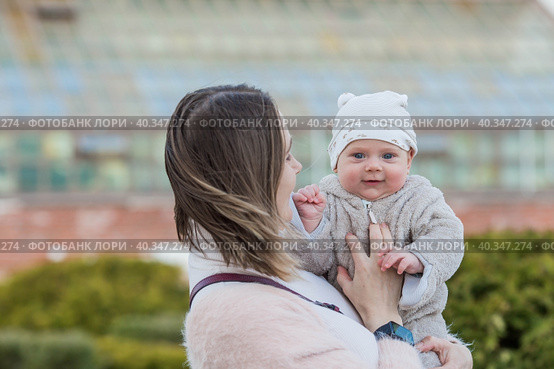 A young mother holds a charming little son in her arms. The kid looks at the camera and smiles. Portrait of a beautiful chubby 4-month-old baby. Стоковое фото, фотограф Photojuli / Фотобанк Лори