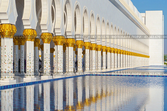 Abu Dhabi, United Arab Emirates - Jan 10 2024, panoramic view of Sheikh Zayed Grand Mosque colonnade with arches and pool on foreground, at daytime, Abu Dhabi, United Arab Emirates. Редакционное фото, фотограф Сергей Богомяко / Фотобанк Лори