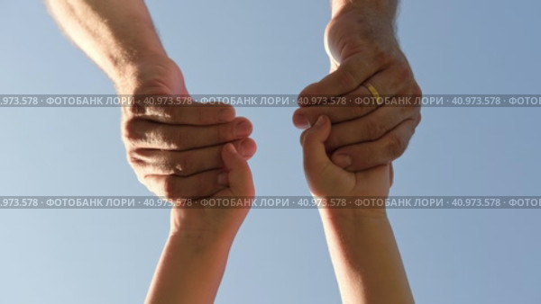 Adult holding a child by the hand on blue sky background. Parent hand reaches out to help child hand in need. Kids Shaking Hands. Children's hand reaches for a daddy. family united. Handshake. Стоковое видео, видеограф Марина Демидюк / Фотобанк Лори