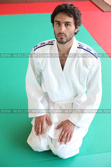 Adult male kneeling on mat in martial arts clothing. Стоковое фото, агентство Ingram Publishing / Фотобанк Лори