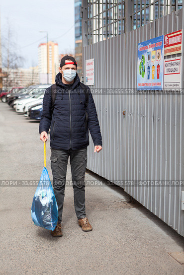 Adult man taking out garbage during coronavirus pandemic, it is allowed without any permission. Inscription on plate in Russian: trush enclosure and attention videosurveillance. Стоковое фото, фотограф Кекяляйнен Андрей / Фотобанк Лори