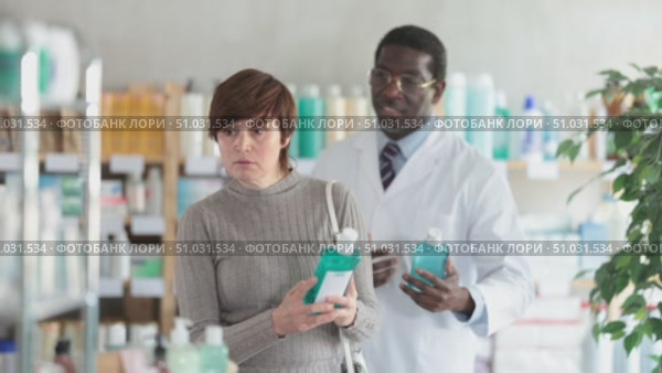 Adult woman buyer choosing bottle of mouthwash with help of adult man pharmacist in pharmacy. Стоковое видео, видеограф Яков Филимонов / Фотобанк Лори