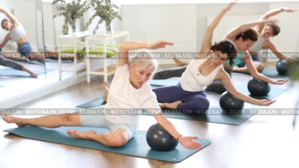 Adult woman doing pilates with soft ball in female group in fitness studio. Стоковое видео, видеограф Яков Филимонов / Фотобанк Лори