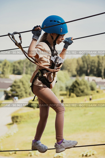 Adventurous Girl Navigating the Rope Park Challenges Under a Bright Sky. Стоковое фото, фотограф Aleksandr Golubev / Фотобанк Лори
