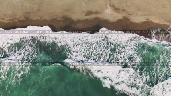 Aerial view capturing emerald green waves breaking over golden sand, white foam cascading along pristine coastal landscape with serene marine scenery. Стоковое видео, видеограф ILIA GOROKHOV / Фотобанк Лори