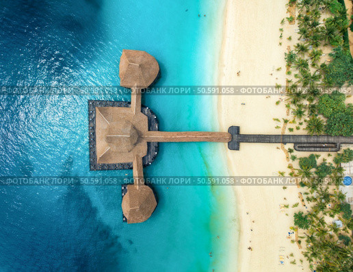 Aerial view of bungalow, white sandy beach, ocean on summer sunny day. Restaurant on the sea. Top drone view of wooden hotel, azure water, green palms. Luxury resort in Kendwa, Zanzibar. Tropical. Стоковое фото, агентство Ingram Publishing / Фотобанк Лори
