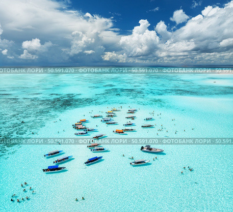 Aerial view of colorful boats and yachts in transparent water on sunny summer day. Mnemba island, Zanzibar. Top view of sandbank in low tide, blue sea, swimming people, yachts, sky with clouds. Ocean. Стоковое фото, агентство Ingram Publishing / Фотобанк Лори