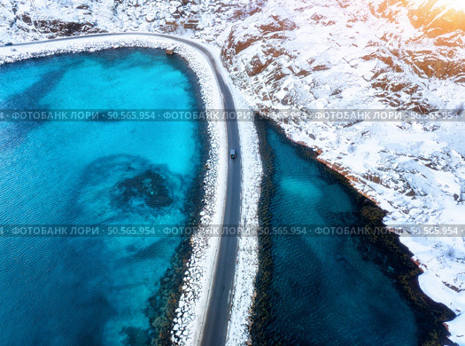 Aerial view of curved snowy road to the island and blue sea at sunset. Highway in snow and azure transparent water. Winter landscape. Top drone view of road in Lofoten islands, Norway. Travel. Стоковое фото, агентство Ingram Publishing / Фотобанк Лори