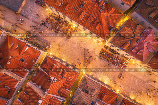 Aerial view of houses with red roofs at night in Dubrovnik, Croatia. Top view of beautiful architecture in old city. City lights, historical centre, buildings, walking people in illuminated streets. Стоковое фото, агентство Ingram Publishing / Фотобанк Лори