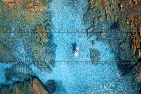 Aerial view of man on sup board in blue sea, rocks at sunset in summer. Man on floating canoe in transparent azure water. Kayak. Sardinia island, Italy. Tropical seascape. Active travel. Top view. Стоковое фото, агентство Ingram Publishing / Фотобанк Лори