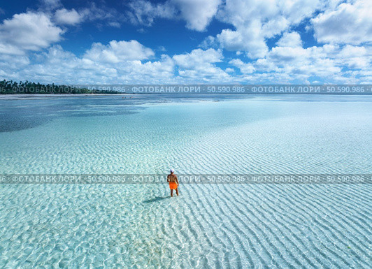 Aerial view of man on the sandbank in ocean, white sand, blue sea during low tide at sunrise in summer. Zanzibar island. Top drone view of guy, sand spit, lagoon, clear water, sky with clouds. Travel. Стоковое фото, агентство Ingram Publishing / Фотобанк Лори