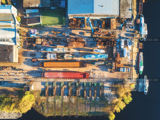 Aerial view of ships and boats in dry dock for repairs. Top view of iron rusting ship is in dry dock for refurbishing. Industrial scene with old yachts, buildings, tree and football field at sunset. Aerial view of ships and boats in dry dock. Aerial view of ships and boats in dry dock. Стоковое фото, агентство Ingram Publishing / Фотобанк Лори