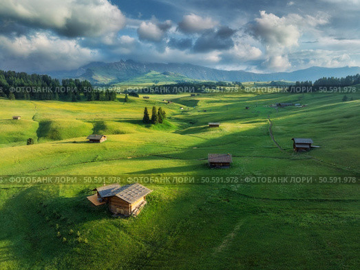 Aerial view of the largest high-altitude alpine meadow in europe, alpe di siusi, wooden huts nestled in a lush green landscape at sunset. Top view of  houses in mountains. Summer in Dolomites, Italy. Стоковое фото, агентство Ingram Publishing / Фотобанк Лори