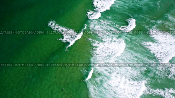 Aerial view of waves of emerald green ocean rolling towards the shore. Unrecognized surfer trying to. Стоковое видео, видеограф Igor Tichonow / Фотобанк Лори