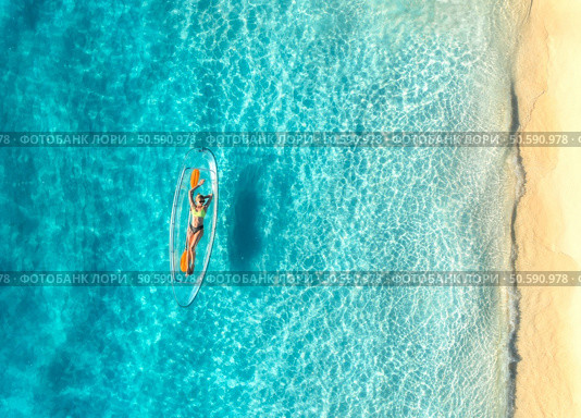 Aerial view of young woman lying on transparent canoe in blue sea at sunset. Summer in Zanzibar. Top drone view of beautiful slim girl, kanoe, sandy beach, ocean with clear water. Tropical background. Стоковое фото, агентство Ingram Publishing / Фотобанк Лори