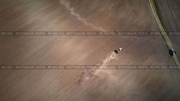 Aerial view plowing the spring field with a tractor, the post drank dragging behind the tractor. On the right side, a dirt road with a parked coarse. Ukraine. Photo from the drone. Aerial view the tractor plows the spring field.spring season of agricultural works at farmlands. Drone photograph. Стоковое фото, агентство Ingram Publishing / Фотобанк Лори