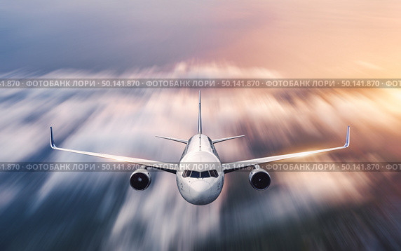 Airplane with motion blur effect is flying over low clouds at sunset. Passenger airplane, blurred clouds, colorful sky at dusk. Aerial view of the modern aircraft. Business travel. Commercial plane. Стоковое фото, агентство Ingram Publishing / Фотобанк Лори