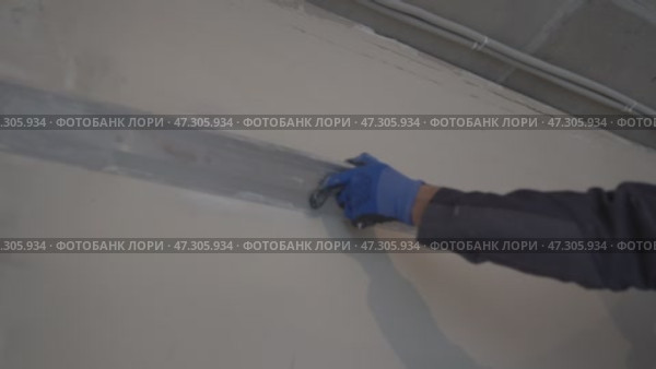 Alignment of the walls near the ceiling. Home improvement. Apartment renovation. Men's hands in protective gloves with a construction metal rule in their hands, Стоковое видео, видеограф Darya Komarova / Фотобанк Лори
