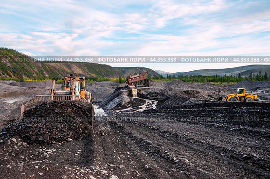 Американский бульдозер CATERPILLAR в горной местности, сгребает от промывочного устройства отработанный горный грунт, чтобы затем его сгрести ковшом в отвал. На дальнем плане - стационарное промывочное устройство для промывки золота (2010 год). Редакционное фото, фотограф Павел Просянов / Фотобанк Лори