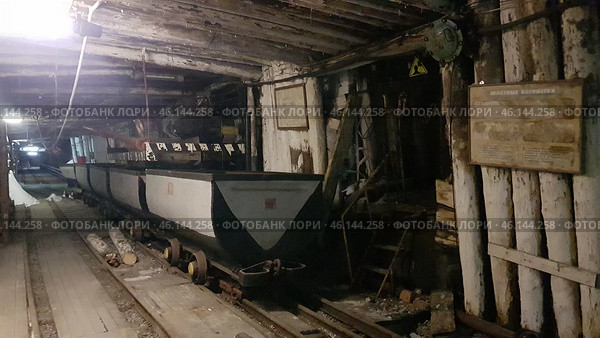 An old mine in Vorkuta, with narrow mine tracks with loaded mine cars on them. You can see the wooden logs that support the tunnel. The walls and ceiling of the mine are dark, covered with soot and traces of dampness, creating the atmosphere of an abandoned or museum object.On the right side there are signs, one of which is called "Mine cars", indicating the museum nature of the exhibition. Above the stairs there is a radiation sign, possibly warning of a possible danger. The stairs lead up into the depths of the tunnel, creating an effect of the unknown.Such mines were key coal mining sites in Vorkuta, playing an important role in the history of the city and the region. This is a reminder of the hard work of the miners, as well as the Gulag era, when prisoners worked in the mines. (2021 год). Редакционное фото, фотограф Анна Кривицкая / Фотобанк Лори