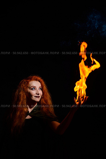 An ominous witch with long curly hair holds a magical fire. Tongues of flame on the palms of a red-haired smirking woman. Witchcraft. Стоковое фото, фотограф Михаил Решетников / Фотобанк Лори