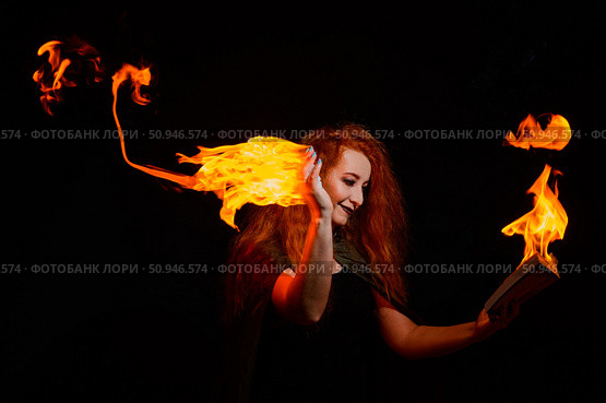 An ominous witch with long curly hair holds a magical fire. Tongues of flame on the palms of a red-haired smirking woman. Witchcraft. Стоковое фото, фотограф Михаил Решетников / Фотобанк Лори