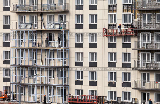 ANGARSK, IRKUTSK REGION, RUSSIA - October 08, 2024: Builders work on a high-rise residential building: tiling the facade, glazing balconies and windows. Housing construction concept. Редакционное фото, фотограф Виктория Катьянова / Фотобанк Лори