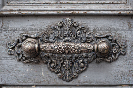 Antique Door Knob. Ornate wooden door with intricate carving metal handle. Faded gray wood. Elaborately fancy cabinet. Old furniture. Traditional architecture design. Decorative wrought iron metalwork. Стоковое AI-изображение, AI-художник Марина Демидюк / Фотобанк Лори