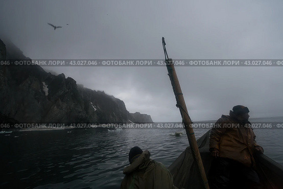 Арктические морские охотники во время традиционной гарпунной охоты на моржей и лахтаков. Берингов пролив, Чукотка, Россия. Холодная июльская ночь в Арктике на Крайнем Севере России. Морзверобои на вельботе много часов терпеливо ждут появления морских животных. Редакционное фото, фотограф Андрей Степанов / Фотобанк Лори