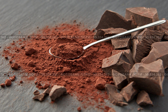Arranged shiny teaspoon on pile of dry cocoa powder and heap of organic chocolate pieces on gray surface. Chunks of chocolate and cocoa powder. Стоковое фото, агентство Ingram Publishing / Фотобанк Лори