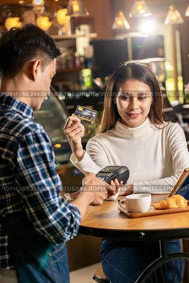 Asian customer using credit card with contactless nfs technology to pay a waiter for coffee purchase at table in cafe. Стоковое фото, агентство Ingram Publishing / Фотобанк Лори