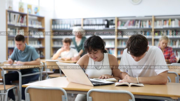 Asian schoolgirl, studying with a classmate guy in the school library on a laptop and making notes in a copybook, preparing for lessons. Стоковое видео, видеограф Яков Филимонов / Фотобанк Лори