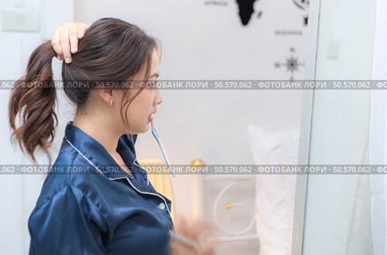 Asian young woman in a blue pajama is brushing her teeth in front of the mirror before taking a shower. Стоковое фото, агентство Ingram Publishing / Фотобанк Лори