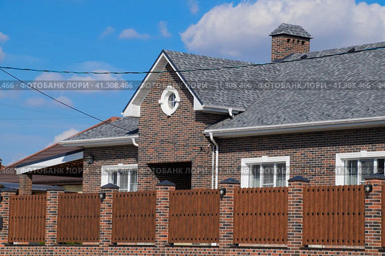 Asphalt shingle. Decorative bitumen shingles on the roof of a brick house. Fence made of corrugated metal. Стоковое фото, фотограф Леонид Еремейчук / Фотобанк Лори