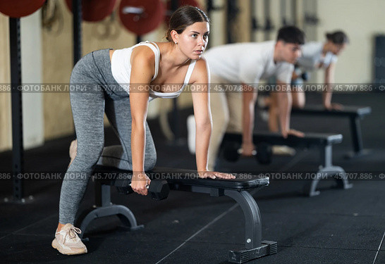 Athletic young woman pumping her biceps with a dumbbell while leaning on bench. Стоковое фото, фотограф Яков Филимонов / Фотобанк Лори
