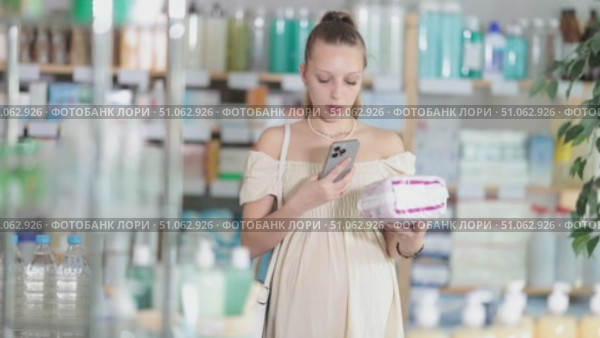 Attentive pregnant woman scanning barcode on feminine pads in chemist's shop. Стоковое видео, видеограф Яков Филимонов / Фотобанк Лори