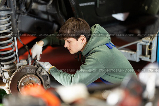 Auto mechanic connects brake hose to front wheel hub of car. Стоковое фото, фотограф Яков Филимонов / Фотобанк Лори