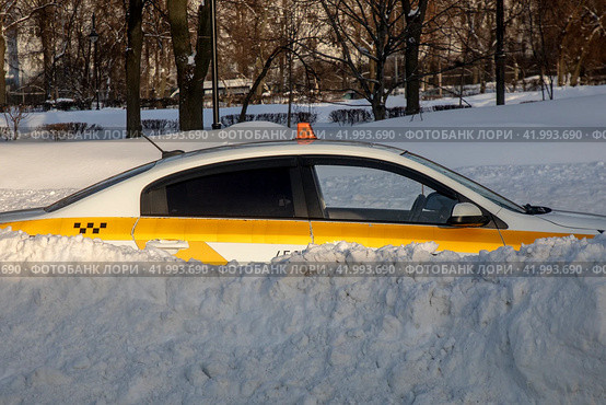 Автомобиль такси занесенный снегом стоит на улице и ждет клиента после сильного снегопада в городе Москве, Россия (2024 год). Редакционное фото, фотограф Николай Винокуров / Фотобанк Лори