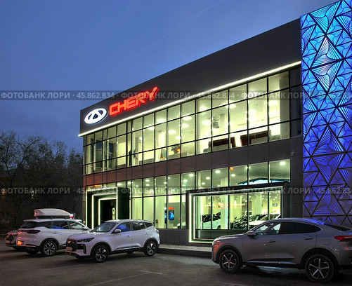 Автосалон CHERY центр OPTIMA в Астрахани ( вид с улицы, при вечернем электрическом освещении ).  Перед центром-новые автомобили. Редакционное фото, фотограф Павел Просянов / Фотобанк Лори