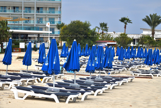 Ayia Napa, Cyprus - November 4. 2018. Empty sun loungers and folded umbrellas on Makronissos Beach Resort. Swimming season ends. Редакционное фото, фотограф Володина Ольга / Фотобанк Лори