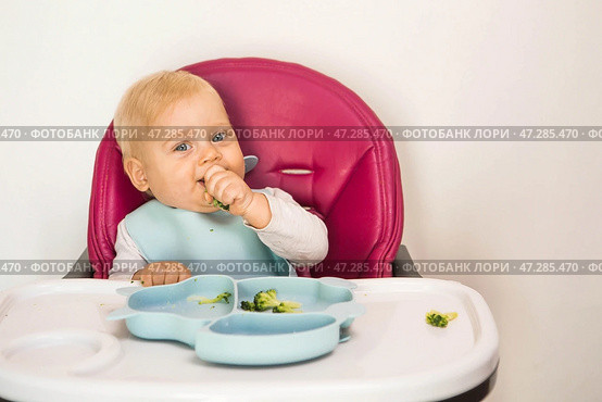 Baby food. The first meal. Feeding the baby. A cute little kid eats vegetables. Healthy food. The child is sitting on a high chair for feeding. Fresh vegetables and fruits. Стоковое фото, фотограф Photojuli / Фотобанк Лори
