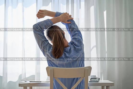 Back view of young faceless woman in casual clothes stretching. Remote work challenges and disadvantages. Working at home difficulties. Downsides of hardworking. Quarantine workspace. Neutral tones. Стоковое фото, фотограф Natalia Gdovskaia / Фотобанк Лори